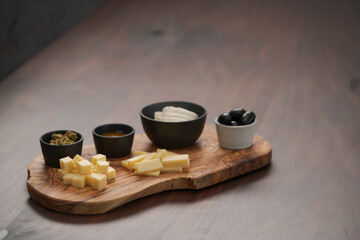 Obraz na płótnie Canvas Wood board with cheese, olives and sauces on walnut table with copy space