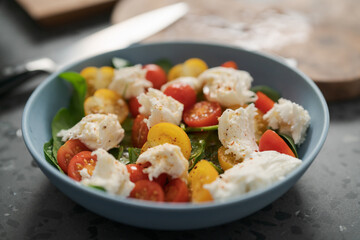 Salad with red and yellow cherry tomatoes , mozzarella and spinach in blue bowl on concrete countertop