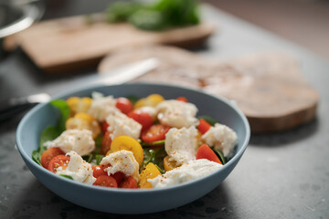 Salad with red and yellow cherry tomatoes , mozzarella and spinach in blue bowl on concrete countertop