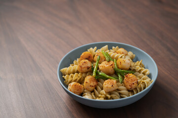 Fusilli pasta with scallops and asparagus in blue bowl on walnut wood surface with copy space
