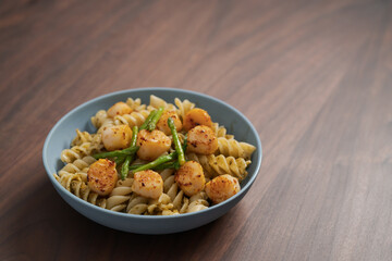 Fusilli pasta with scallops and asparagus in blue bowl on walnut wood surface with copy space