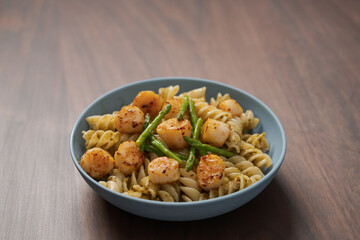 Fusilli pasta with scallops and asparagus in blue bowl on walnut wood surface with copy space
