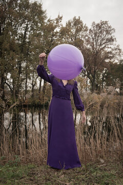 Woman in purple dress holding a large violet balloon outdoors in nature in autumn or winter