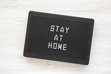 'Stay at home' words on a black lightbox on a white wooden surface, overhead view. Top view, from above, flat lay.