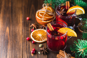 Obraz na płótnie Canvas Hot wine drink with spices and fruits in a glass on a wooden background, branches of a Christmas tree and oranges, copy space. Christmas mulled wine or punch.