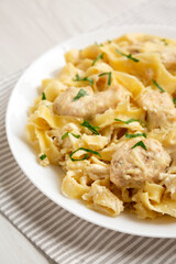 Homemade Chicken Fettuccine Alfredo in a plate on a white wooden surface, side view.