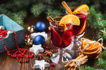 Hot wine drink with spices and fruits in a tall glass and a box with toys for the Christmas tree on the background. Fragrant, hot punch or mulled wine for Christmas.