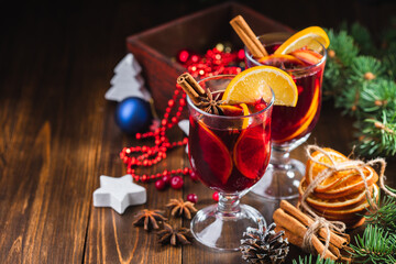 Obraz premium Hot Christmas drink of wine, fragrant spices and fruits in a glass on a wooden rustic background with Christmas decorations. Holiday hot mulled wine or punch.