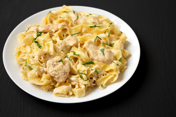 Homemade Chicken Fettuccine Alfredo on a white plate on a black background, side view. Copy space.