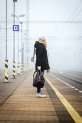 Woman with backpack waiting at railroad station for train. Foggy atmospheric mood in city