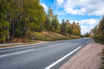 Fototapeta premium View of the highway road in the fall. Traveling background. Asphalt highway passing through the forest. Latvia. Baltic.