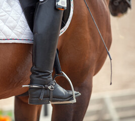 Croup of a red horse with a white saddle and a rider’s foot in a boot with a spur inserted in a...
