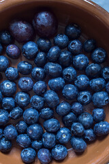 Handmade clay bowl with tasty dark blue blueberries and two black grapes. Recipes and vegetarian food with fruits.