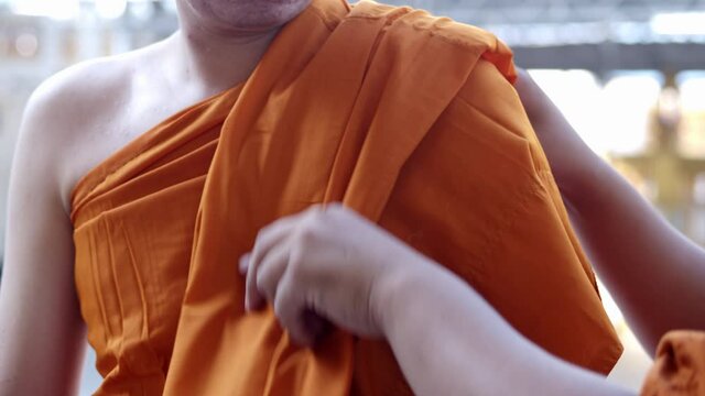 A man is ordaining a new monk in Theravada Buddhism in Thailand changing clothes, becoming covered with Buddhist monk's robe especially.