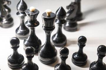 Wooden chess pieces. Black king Queen surrounded by her large retinue, full set of black side chess game, bright light from left, profile view