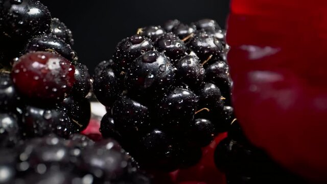 Moving close up shot through fresh raspberries and blackberries with black background shot in 4k 