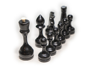 Wooden chess pieces. black pawns stand one after another, looking out from behind their comrades on a white background, focus on the second row of pawns, next to their main comrades, king, Bishop, kni