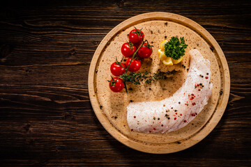 Fresh raw cod loin with seasonings and vegetables served on cutting board on wooden table
