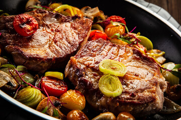 Pork steaks in frying pan with champignons, onion and tomatoes

