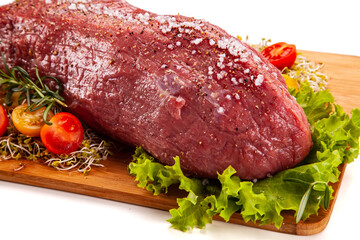 Fresh raw beef on cutting board with fresh vegetables on white background
