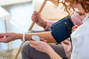 Obraz premium Nurse measuring blood pressure of senior woman at home. Smiling to each other. Young nurse measuring blood pressure of elderly woman at home. Doctor checking elderly woman's blood pressure