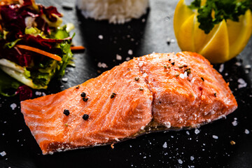 Oven baked salmon steak with white basmati rice,  lemon and fresh vegetable salad served on black...
