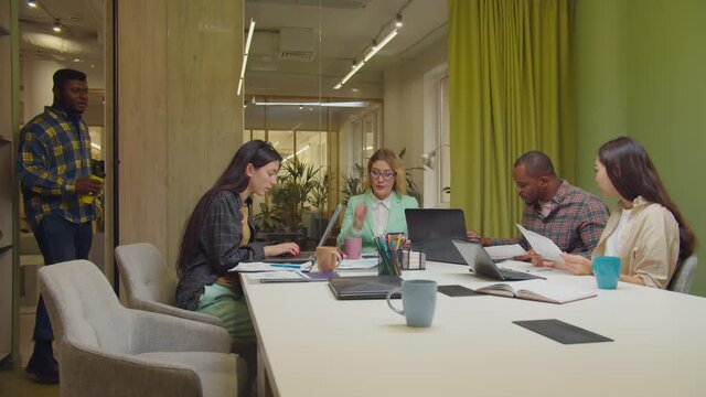 Displeased female executive scolding male african worker for being late on business meeting, giving rebuke while successful diverse multiracial business team working on business project in boardroom.
