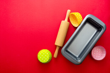 Baking utensils, rolling pin, cupcake molds and aluminium cake mold, red background with copy space. Abstract baking concept.