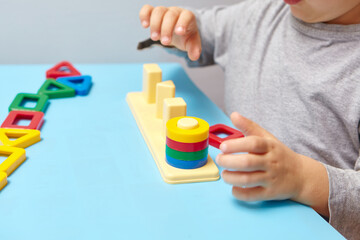 The child collects a sorter. Educational logic toys for kid's. Children's hands close-up. Montessori Games for Child Development. Multicolored logic sorter on white background.