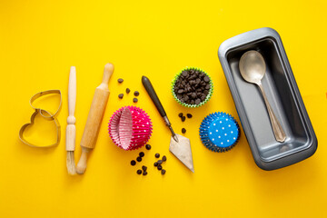 Abstract baking concept. Cooking utensils, rolling pin, cupcake molds, cookies cutters over yellow background flat lay
