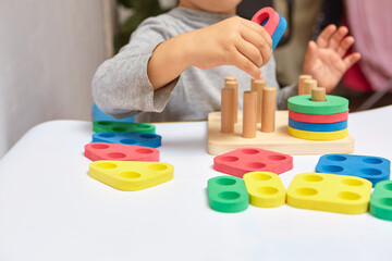 The child collects a sorter. Educational logic toys for kid's. Children's hands close-up. Montessori Games for Child Development. Multicolored logic sorter on white background.