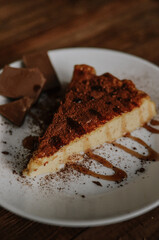 Delicious slice of coffee cheesecake covered with cacao on white plate with caramel and chocolate  on dark wooden background close up