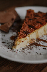 Tasty slice of coffee cheesecake covered with cacao on white plate with chocolate and caramel on dark wooden background close up