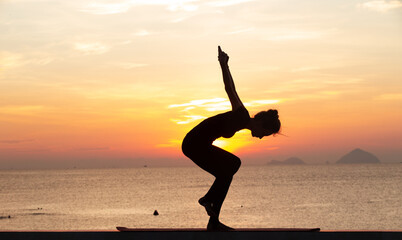 Silhouette of a young woman doing yoga near the sea at sunset.