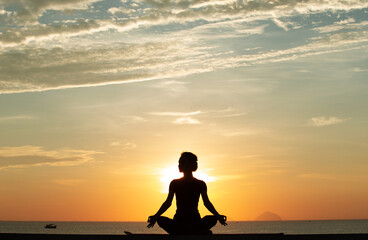 Silhouette of a young woman doing yoga near the sea at sunset.