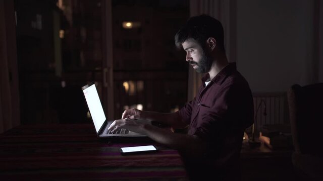 Young professional man working from home with his laptop and receiving a call at late hour at night