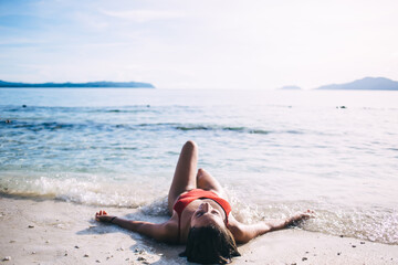Young brunette in red swimsuit lying on sea beach