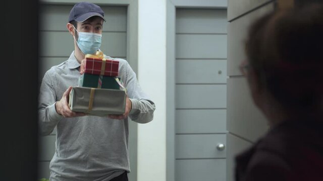 Postman Delivering Christmas gifts to a lady. Courier service during Coronavirus X-mas. Social distance measures transporting parcels.