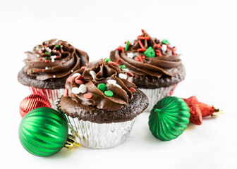 Trio of Christmas Chocolate cupcakes on a white background with ornaments.
