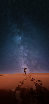 Astrophotography picture with a woman silhouette on a dessert, with milky way on the night sky.