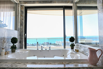 Hot tub near the window with sea view of luxurious hotel room.