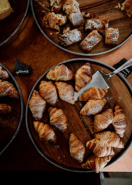 Metal dishes loades with fresh croissants and cakes seen from above on wooden table