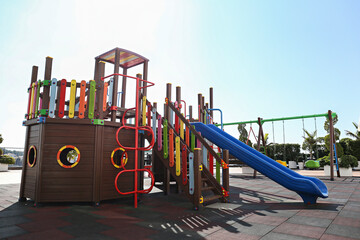 Empty children;s playground with colorful swings and slides on foamy rubber tiles flooring. Copy...
