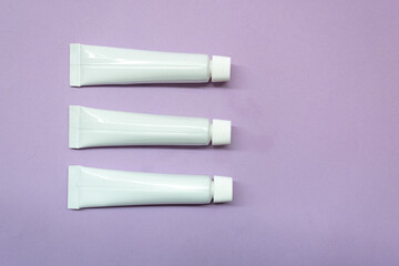 White tubes for cosmetics on a lavender background. Flatley.