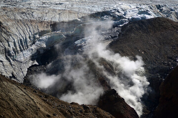 Mutnovsky volcano. A large snowfield on the mountainside. Steaming fumaroles in the crater of the active volcano