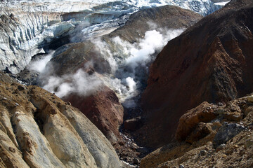 Mutnovsky volcano. A large snowfield on the mountainside. Steaming fumaroles in the crater of the active volcano