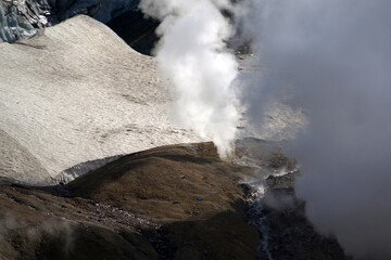 Mutnovsky volcano. A large snowfield on the mountainside. Steaming fumaroles on the banks of the...