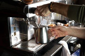 Closeup female hands are making coffee using professional metal machine in cafe.