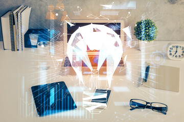 Computer on desktop in office with bulb icon hologram. Double exposure. Concept of idea.