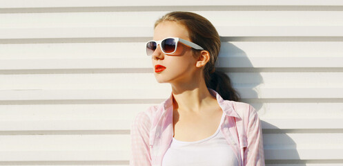 Portrait of young woman wearing a white shirt, sunglasses over background